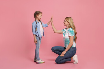 Mother and daughter giving high five on pink background