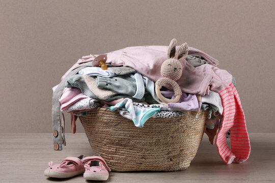 Laundry Basket With Baby Clothes And Shoes On Wooden Table