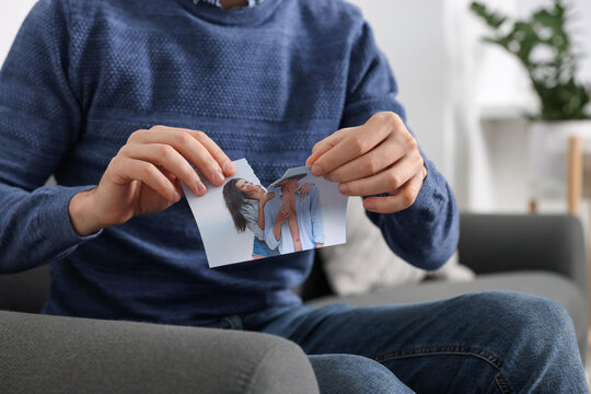 Man ripping photo on sofa indoors, closeup. Divorce concept