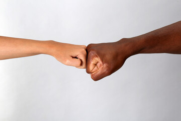 Fototapeta premium Woman and African American man making fist bump on light grey background, closeup