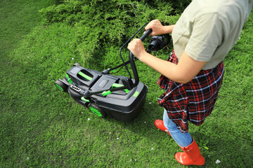 Woman cutting grass with lawn mower in garden, closeup