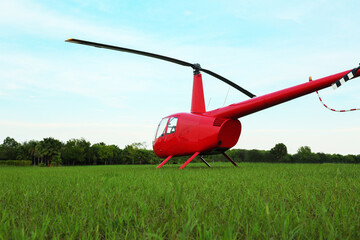 Naklejka na ściany i meble Modern red helicopter on green grass outdoors, low angle view