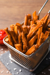 Frying basket with sweet potato fries on wooden table, closeup