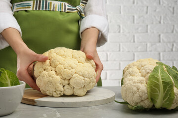 Woman with fresh cauliflower at light grey table, closeup