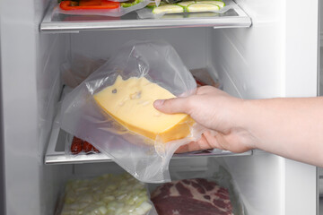Woman putting vacuum bag with cheese into fridge, closeup. Food storage