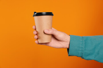 Woman holding takeaway cup with drink on orange background, closeup. Coffee to go