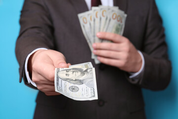 Man holding money on light blue background, closeup. Currency exchange