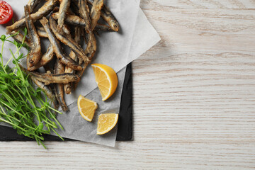 Slate board with delicious fried anchovies, lime and tomatoes on white wooden table, top view. Space for text