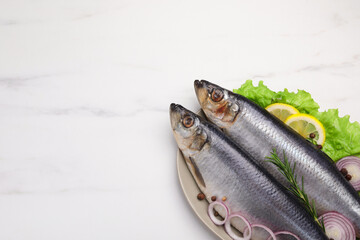 Plate with salted herrings, onion rings, slices of lemon, peppercorns and lettuce on white marble...