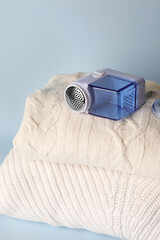Modern fabric shaver and knitted clothes on light blue background