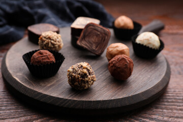 Different tasty chocolate candies on wooden board, closeup