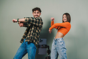 Dancing two young woman and man bloggers recording video in studio isolated over gray background....