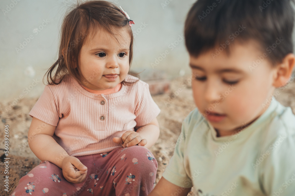 Wall mural a cute baby girl with her brother playing with sand on playground in the weekends. plays. outdoor ac