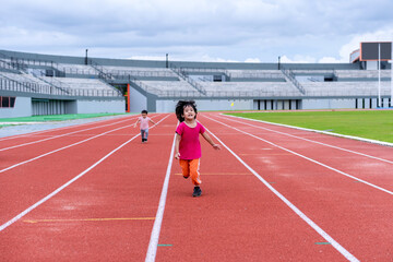 Fototapeta premium A girl in a pink sportswear and sneakers runs on the running track at the stadium outdoors.