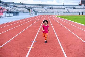 A girl in a pink sportswear and sneakers runs on the running track at the stadium outdoors.