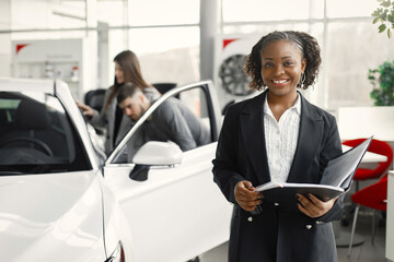 Black saleswoman standing at auto showroom and looking at camera - obrazy, fototapety, plakaty
