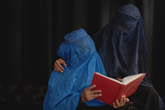 Two Afghan Muslim Women With Burka Traditional Costume, Talking About Holy Quran Against The Dark Background