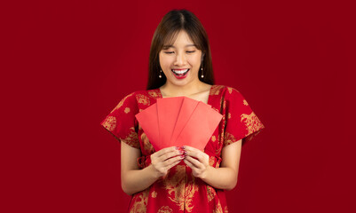 Young asian girl in red chinese style dress smiling and happy face holding red money envelopes red background. Happy Chinese New Year concept.