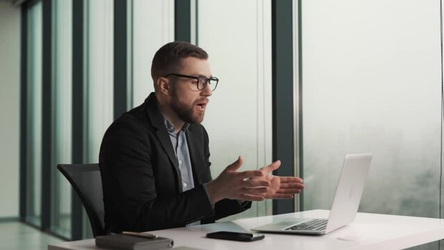 An upset male office worker excuses himself over a laptop video call