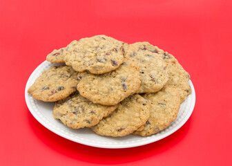 Close up on one porcelain plate full of Oatmeal Cranberry cookies on a red background.