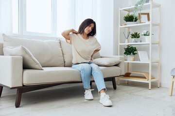 Woman sitting on sofa at home back and lower back pain, protrusion, back problems after 30 years