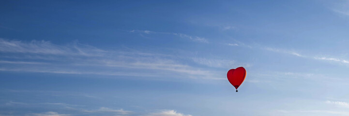 A colorful balloon in the shape of a heart, flying at sunset across the blue sky. Happy Valentine's Day Concept. Banner, space for text.