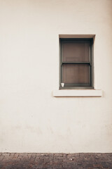 Small window with green trim on white stucco wall. Small cup sitting on window sill. Vertical color photo. 