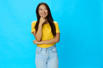 Fototapeta na wymiar Asian woman smiling with teeth in yellow T-shirt and blue jeans on blue background, copy space