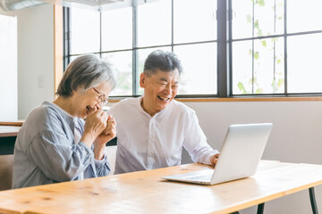 家のダイニングでパソコンを使う高齢者夫婦
