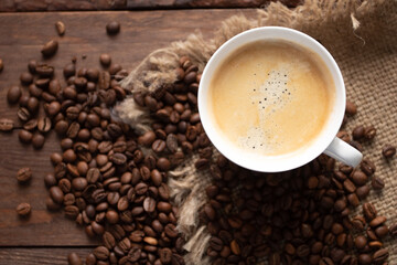 Cup of freshly brewed coffee on wooden table with roasted coffee beans