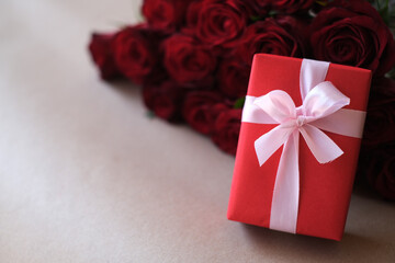 Close up red gift box with bunch of rosy roses blurred background. Valentine's day, wedding, birthday and special occasion concept. Copy space for text.