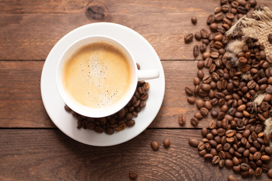 Cup of coffee on wooden table with roasted coffee beans on wooden background. © epovdima
