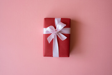 Red gift box with ribbon isolated on pink background for giving in holidays with copy space for text. Holidays, present, giving concept. New year day, Christmas day, Chinese New Year day, Birthday.