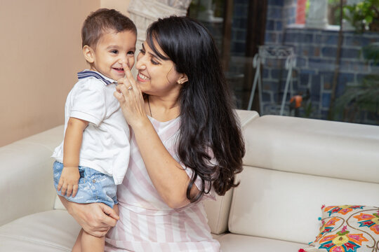 Beautiful young happy indian mother playing with her cute baby boy while standing at home indoors. Asian Mom cuddling little son and expressing unconditional love, Portrait of motherhood.