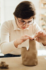 A beautiful young woman shaping a vase from clay in a pottery studio.