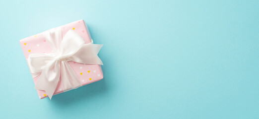 Valentine's Day concept. Top view photo of pastel pink giftbox with white ribbon bow on isolated light blue background with copyspace