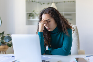 Exhausted Asian businesswoman having a headache in office. Creative woman working at office desk feeling tired. Stressed casual business woman feeling head pain while overworking on laptop computer.