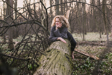 Curly haired lady resting on tree trunk scenic photography. Picture of person with wild wood on background. High quality wallpaper. Photo concept for ads, travel blog, magazine, article