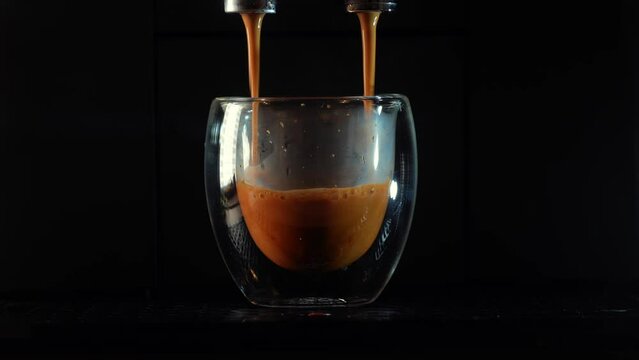 Making an espresso coffee in a double-walled glass cup at a coffee machine. Coffee pouring in the glass cup and the layers of foam are going up. 4k close up video.