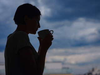 silhouette of a woman with a mug of tea on the background of the city.