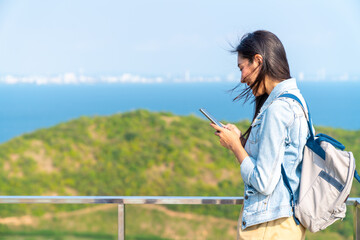 Young Asian woman tourist using mobile phone booking hotel or online shopping during travel at tropical island in summer sunny day. Attractive girl enjoy outdoor lifestyle in beach holiday vacation.