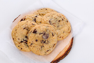 Homemade stacked chocolate chip cookies on wooden plate and white background
