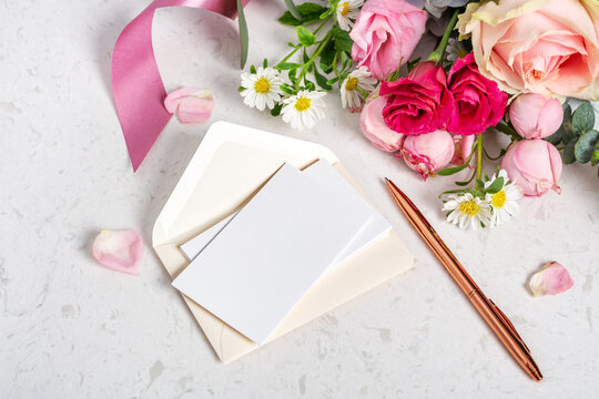 Wedding invitation card, blank card and envelop mockup with rose gold pen on marble table with bunch of flowers