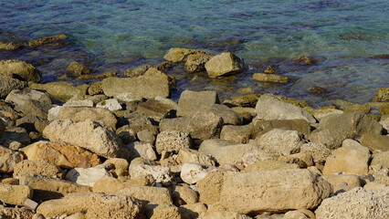 Fototapeta na wymiar Cobble pieces of marble rock near water edge in Caesarea Maritima National Park, Israel.