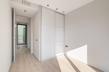 Empty clean bright bedroom with light wooden parquet and white wardrobe with sliding doors. A...