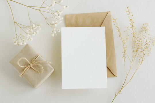 Greeting card mockup, envelope, gift box and  dried gypsophila flowers twigs on beige background top view flatlay. Card mockup with copy space.