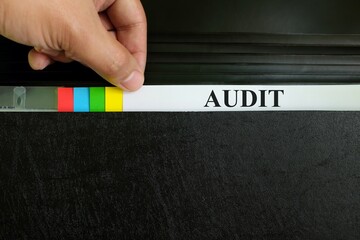 Hand picking audit file record in black binder folder. Auditing in company organization concept.