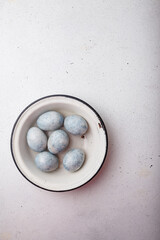 Easter eggs painted blue in white bowl on wooden background. Vertical shot, top view, copy space