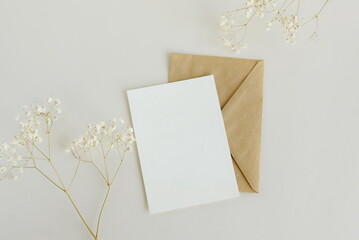 Greeting card mockup, envelope and  dried gypsophila flowers twigs on beige background top view...