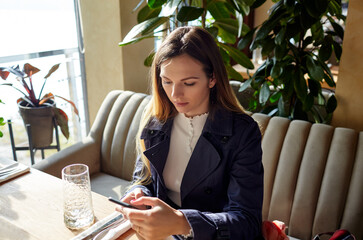 Beautiful attractive woman waiting for coffee in cafe. Coffee break. Morning light falls from the window